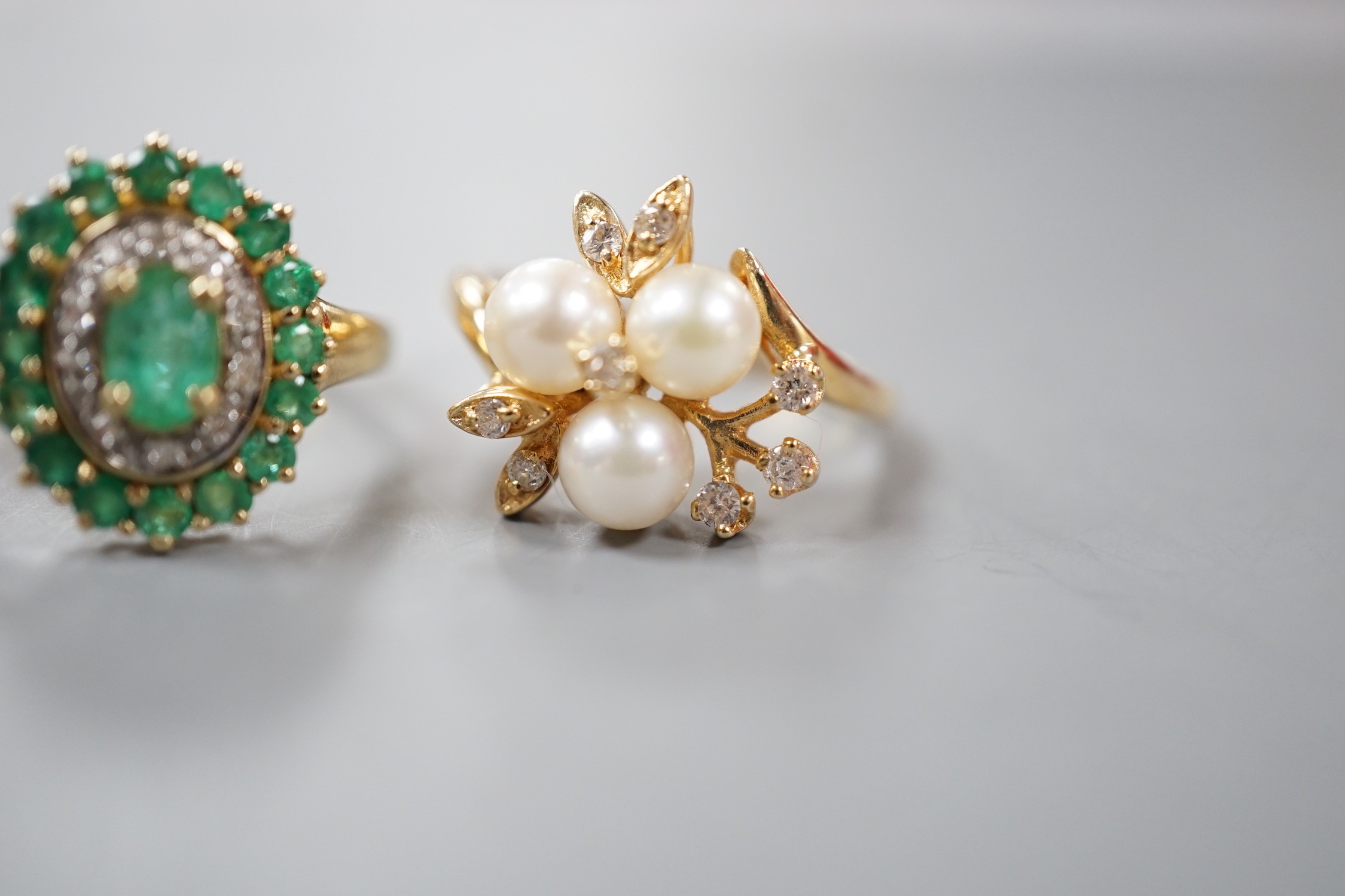 A modern yellow metal, cultured pearl and diamond chip set flower head cluster ring, size K and a 9ct, emerald and diamond chip set cluster ring, gross weight 6.8 grams.
